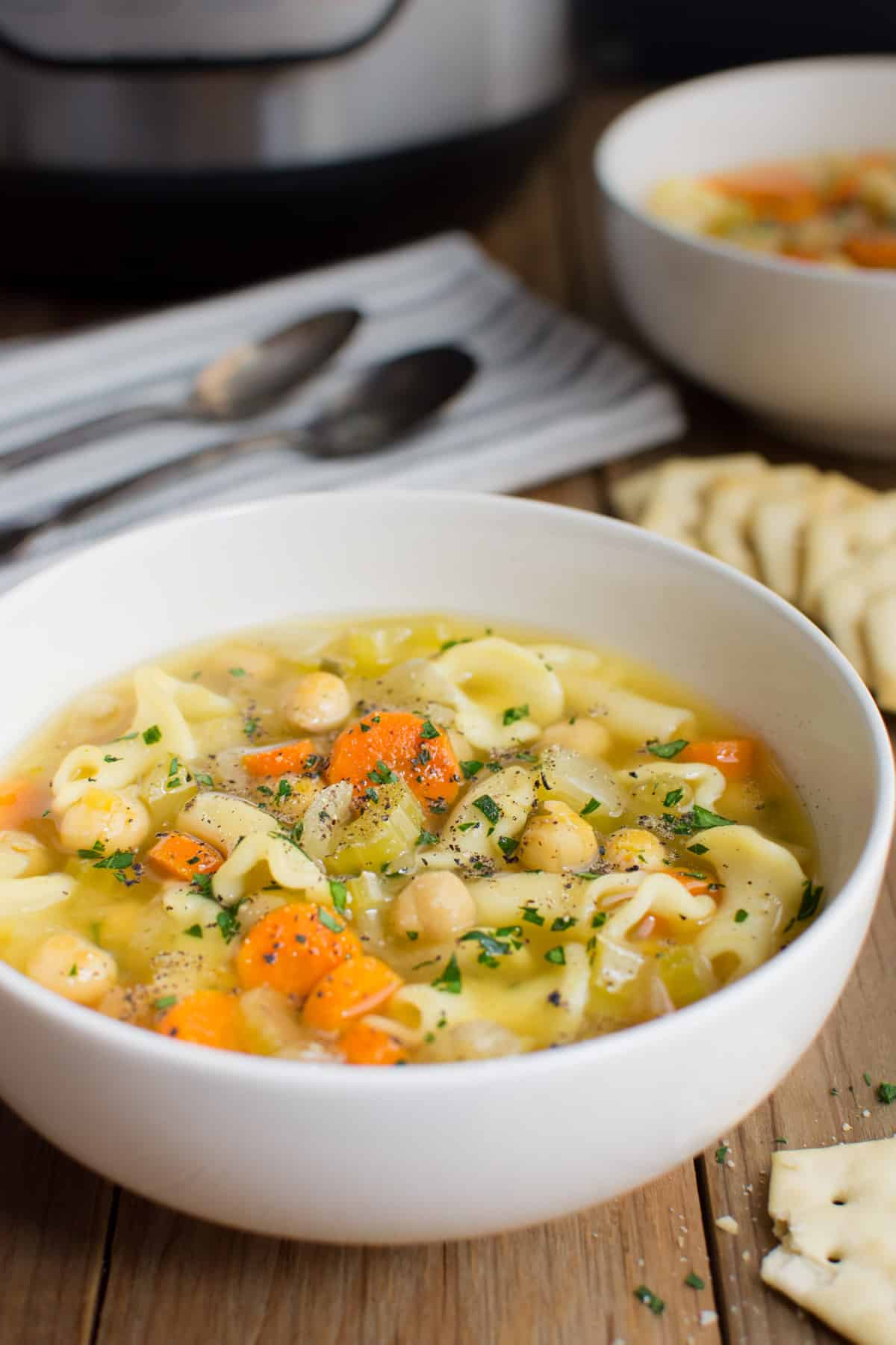 Vegan chickpea noodle soup in a white bowl with a spoon and the Instant Pot in the background.