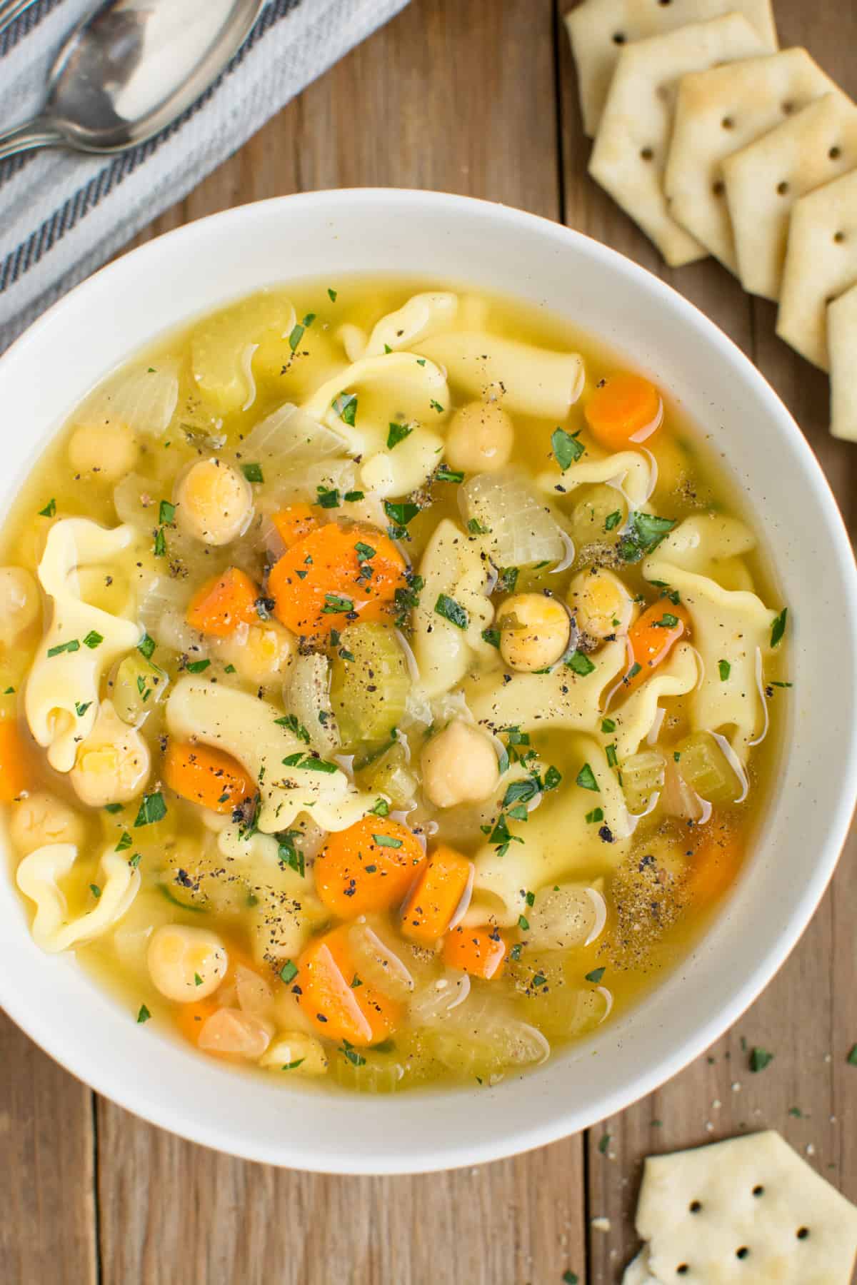 Looking down on a bowl of chickpea noodle soup in a white bowl with crackers on the side.