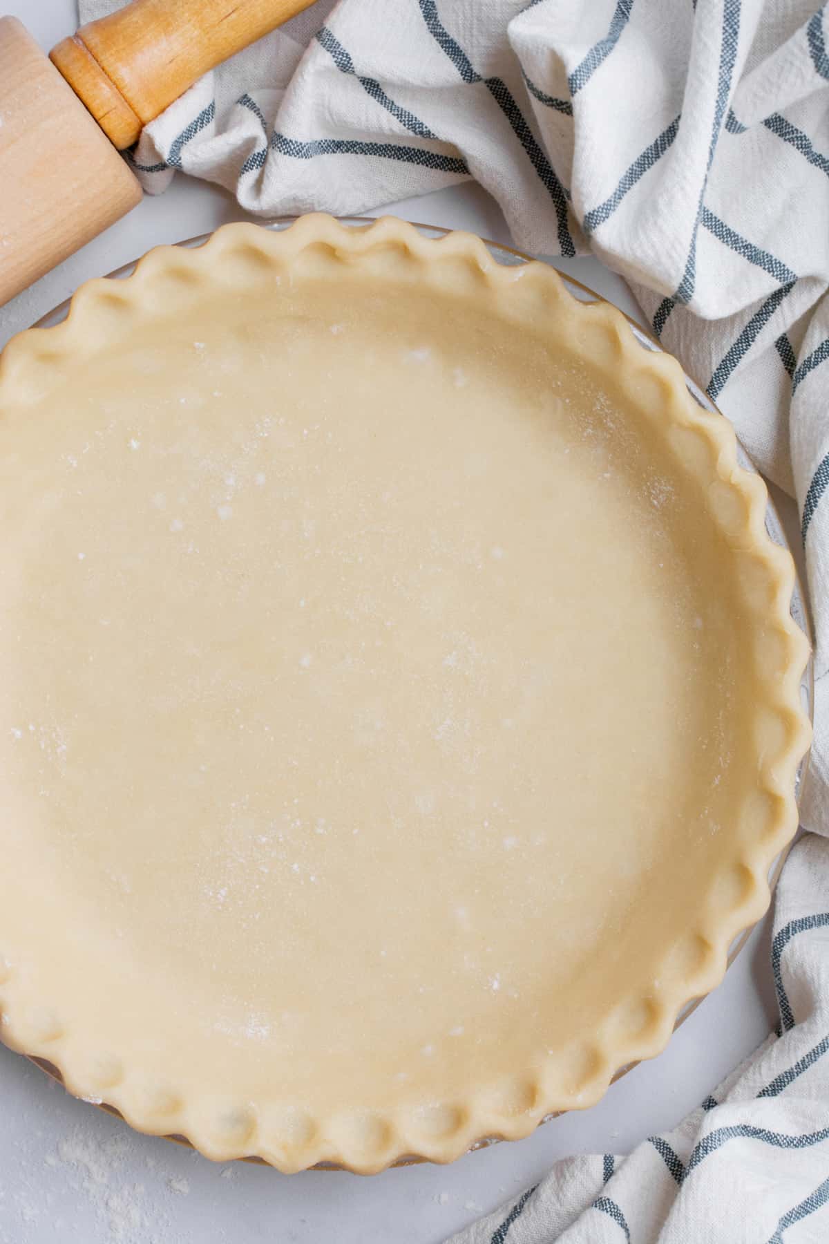 Uncooked homemade vegan pie crust with a kitchen towel and rolling pin nearby.