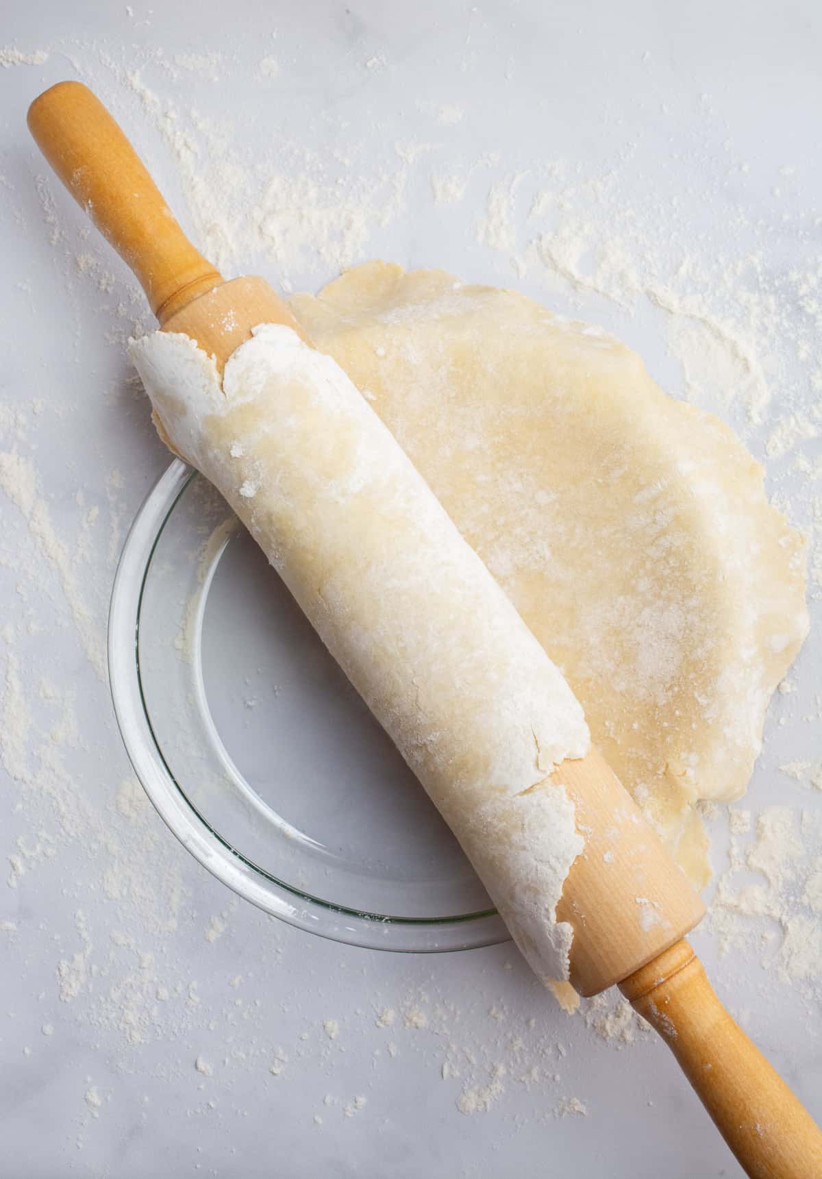 Pie dough being unrolled from a rolling pin over a pie plate.