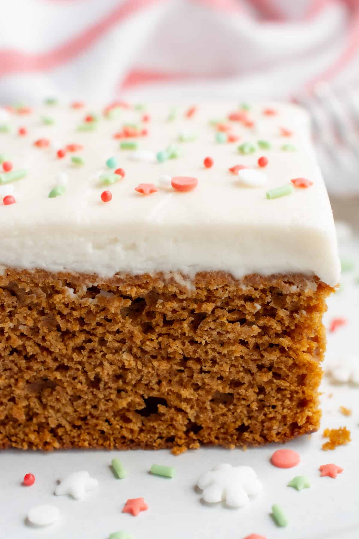 Close up of a slice of vegan gingerbread cake topped with frosting and sprinkles.