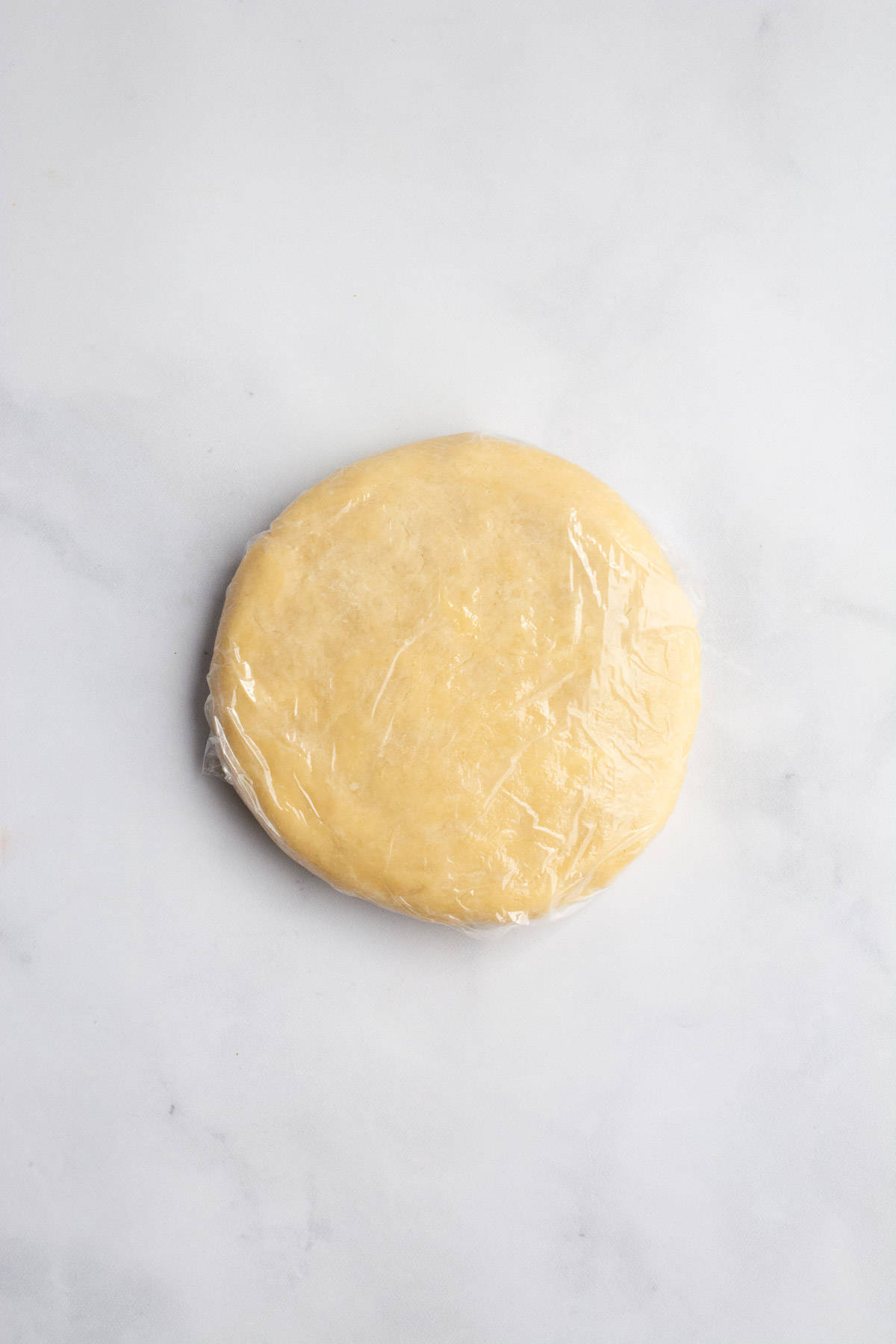 Flattened pie dough wrapped in plastic wrap.