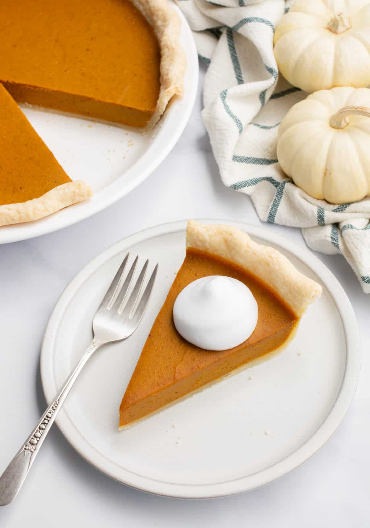 Vegan pumpkin pie with a slice cut out and on a plate topped with coconut whip.