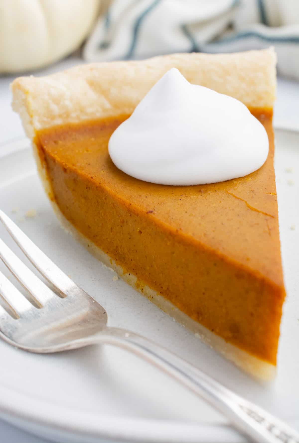 A slice of homemade vegan pumpkin pie topped with coconut whip.