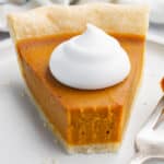 A slice of pumpkin pie topped with coconut whip and a piece taken off with a fork.