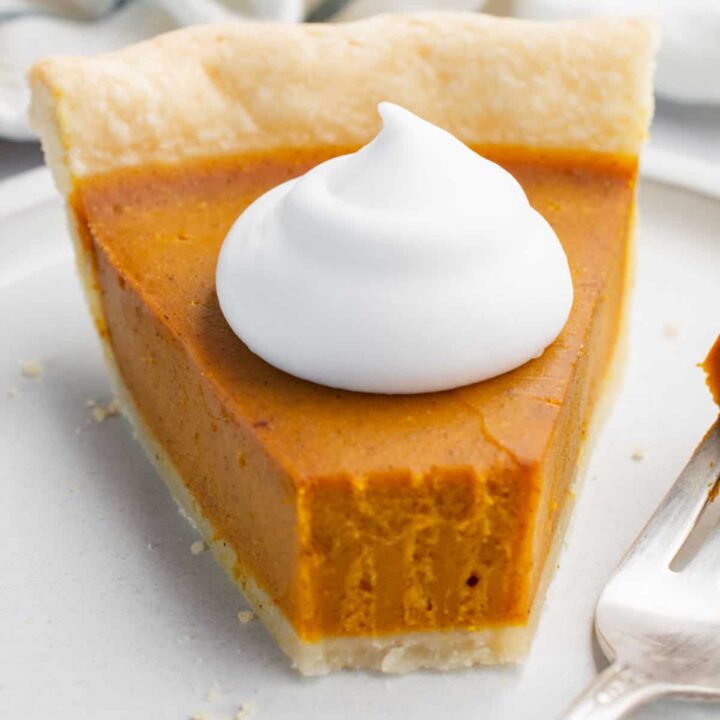A slice of pumpkin pie topped with coconut whip and a piece taken off with a fork.