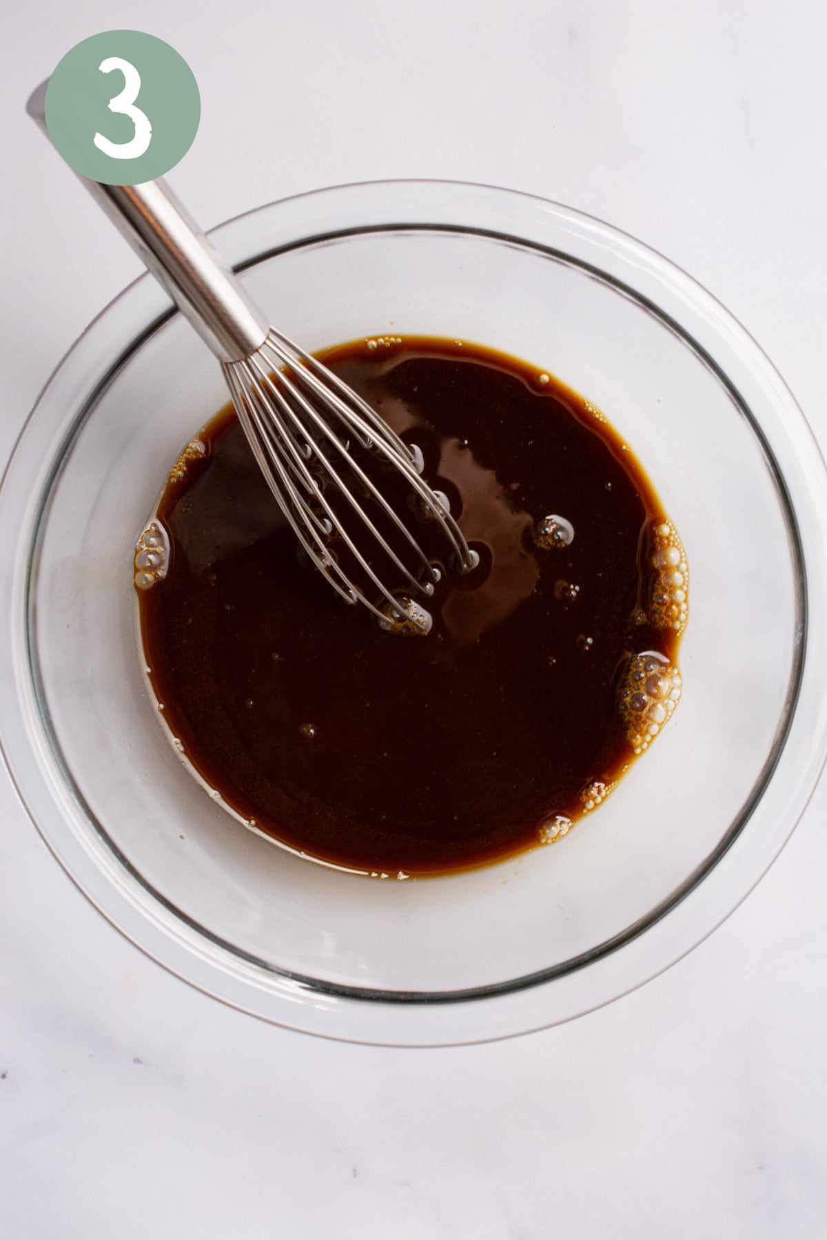Non-dairy milk and molasses mixed in a glass bowl with a whisk.
