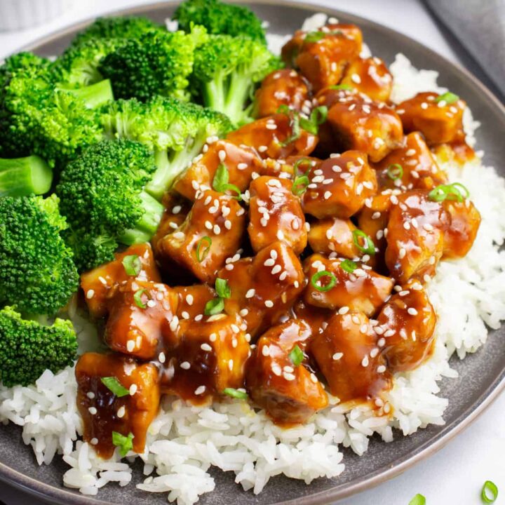 A bed of white rice topped with teriyaki tofu and steamed broccoli on a gray plate.