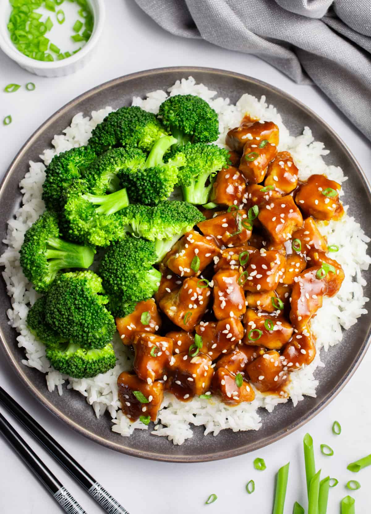 A gray plate of white rice topped with half teriyaki tofu and half steamed broccoli.
