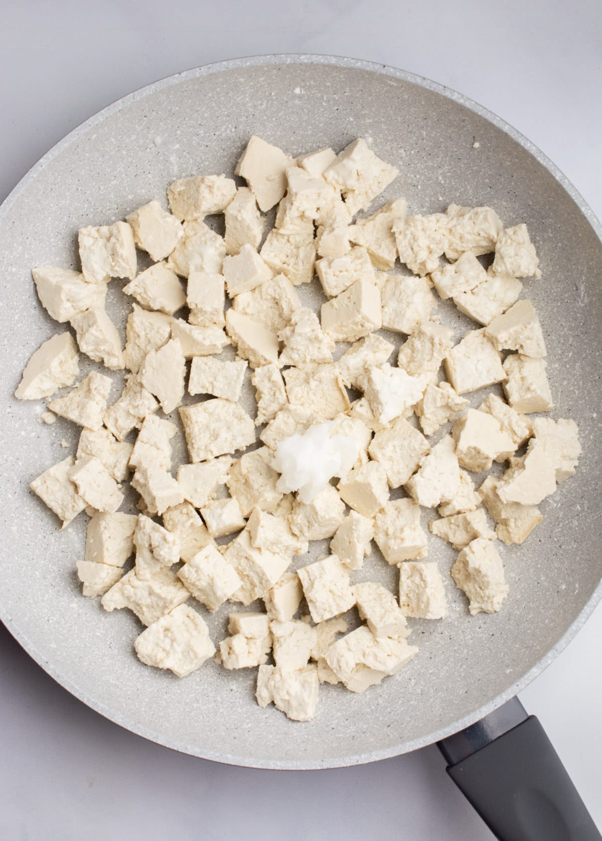 Bite sized tofu pieces in a pan with oil.