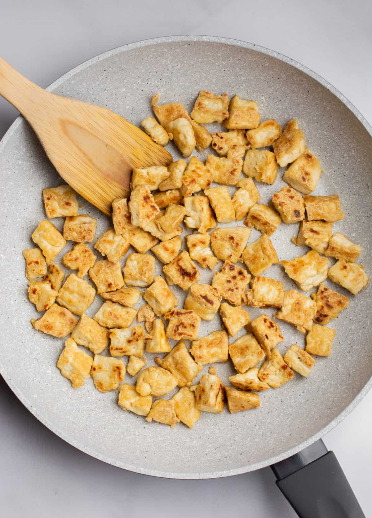 Bite sized pieces of pan fried tofu in a pan with a spatula.