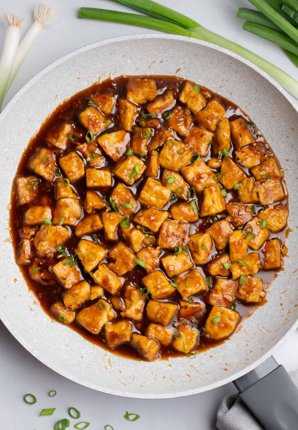 A pan of teriyaki tofu topped with slices of green onion.