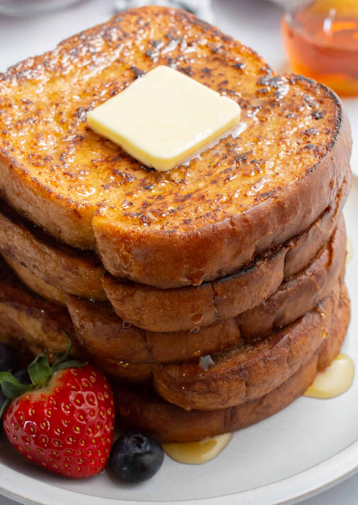 Vegan french toast topped with maple syrup and butter with a side of berries.