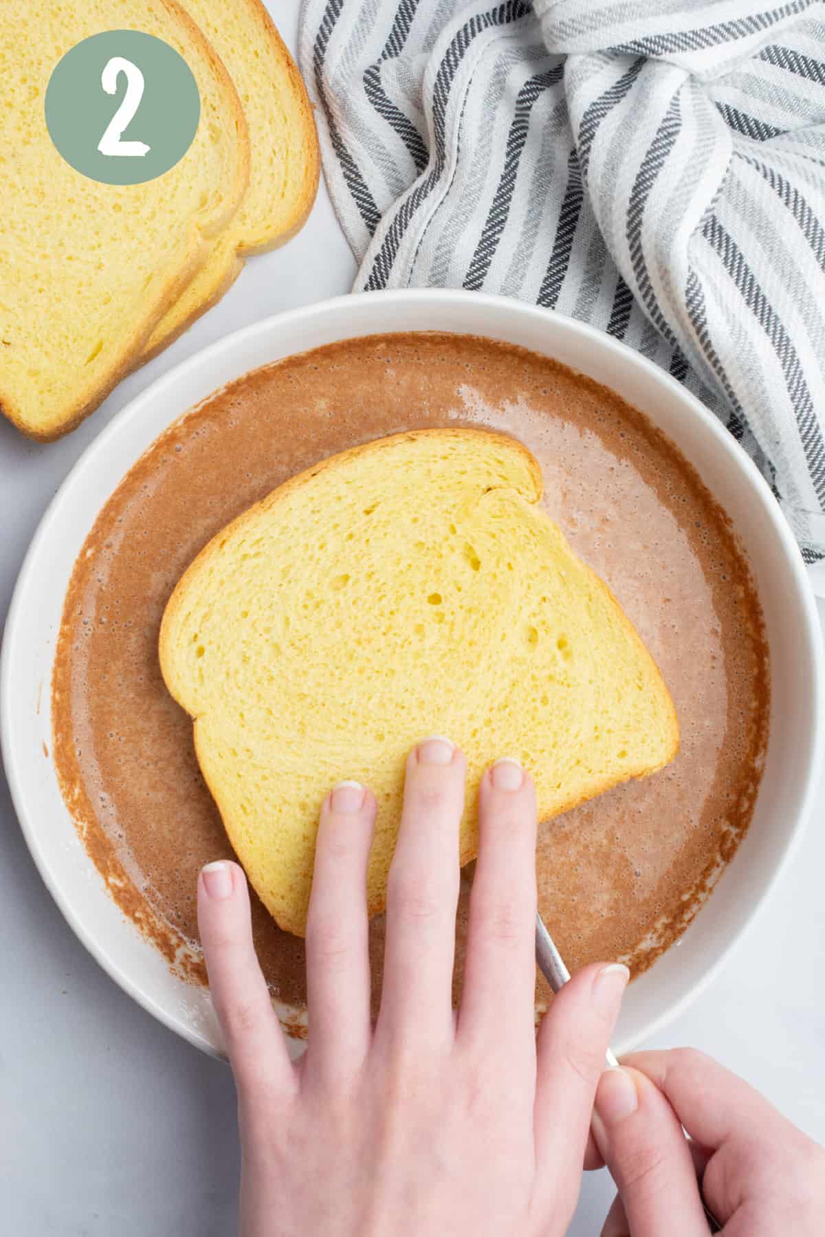 Hands using a fork to help dip a slice of bread in batter.