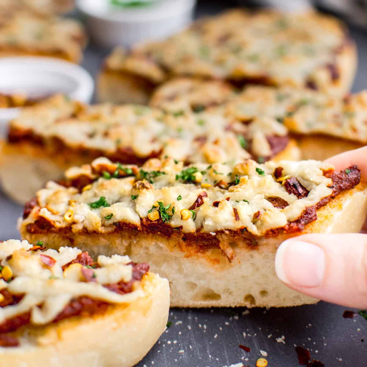 A hand grabbing a slice of vegan french bread cheese pizza.
