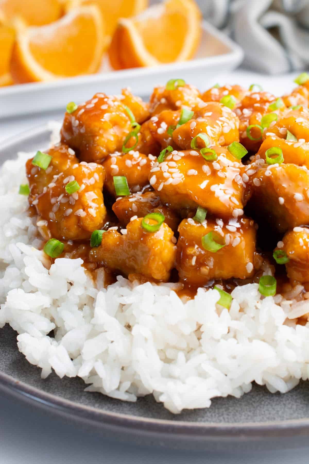 A plate of orange tofu on top of white rice with sesame seeds and chopped green onions.