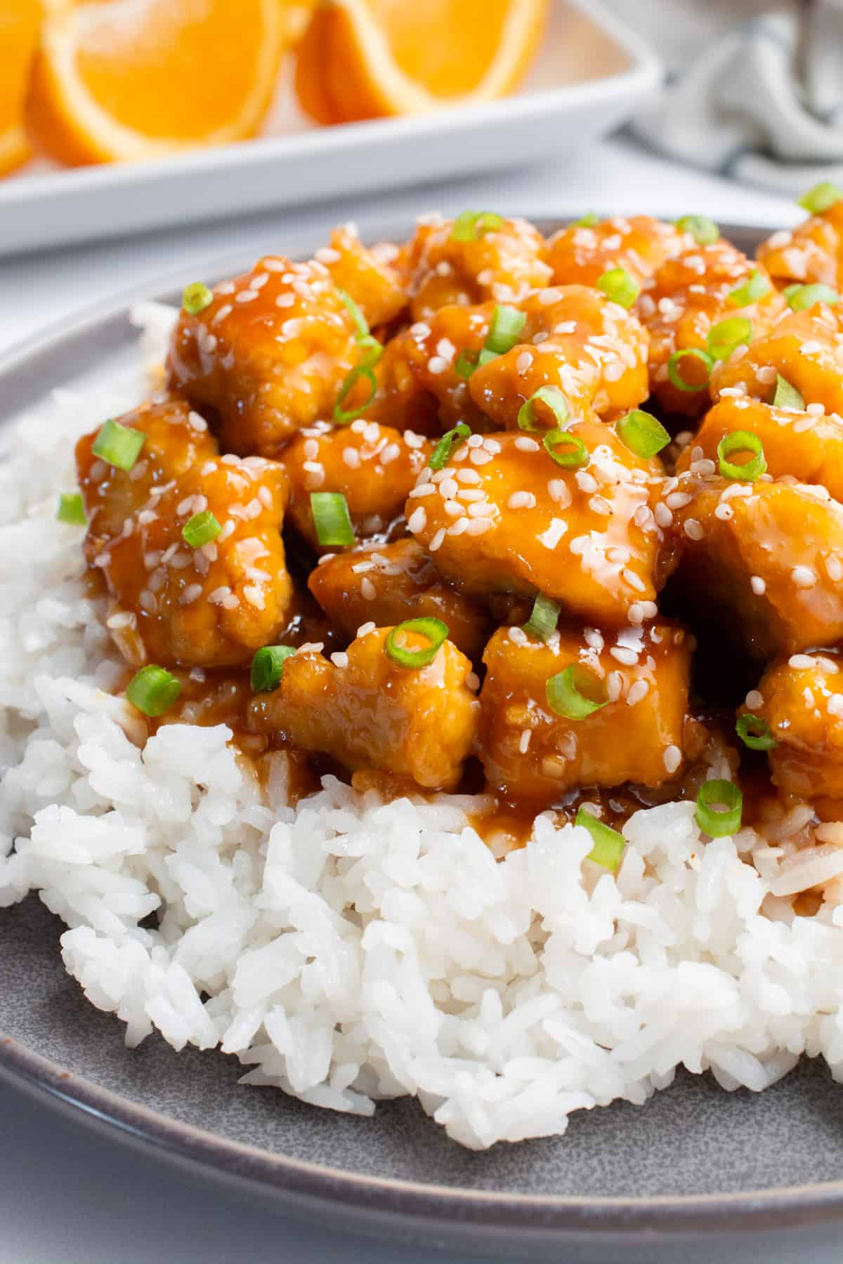 Orange tofu on a bed of white rice topped with sesame seeds and chopped green onions.