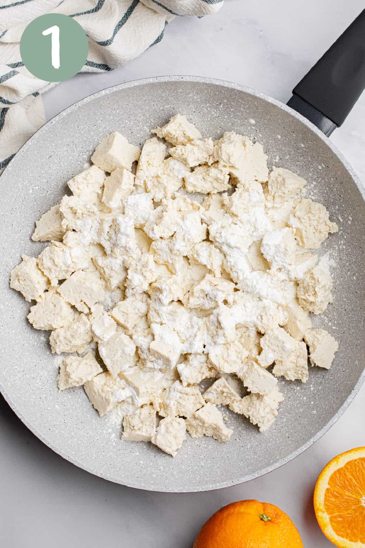 A frying pan with pieces of uncooked tofu sprinkled with cornstarch.