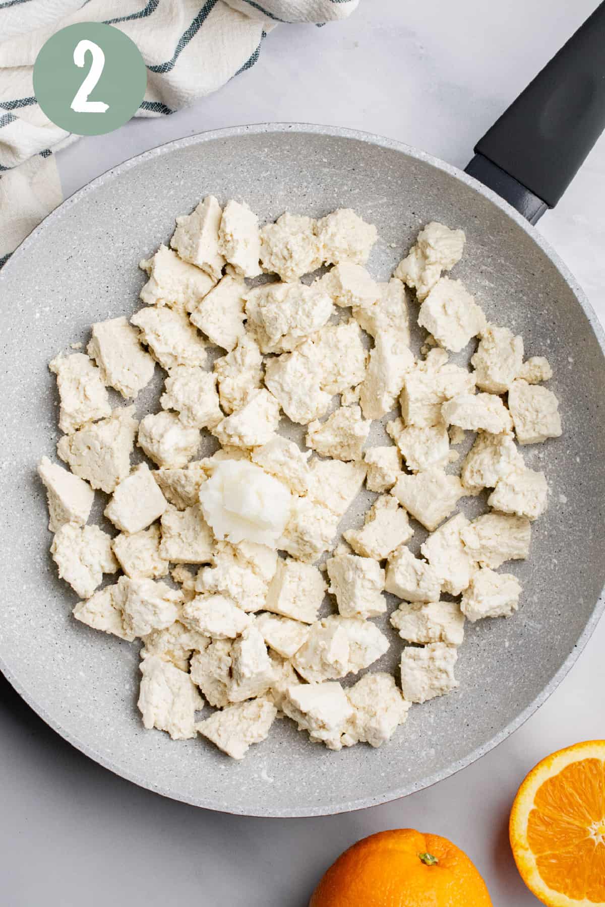 A frying pan with pieces of uncooked tofu and a dollop of coconut oil.