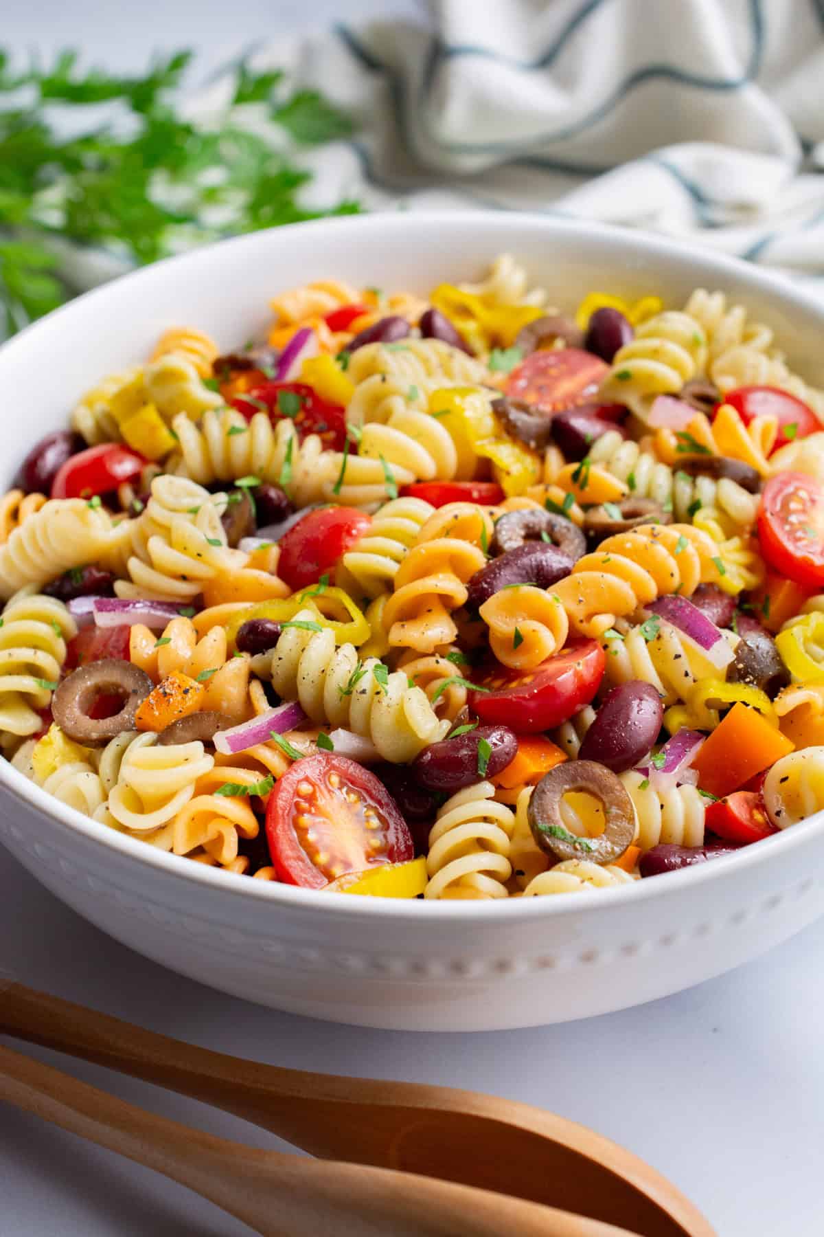 Italian pasta salad in a white bowl with wooden tongs.