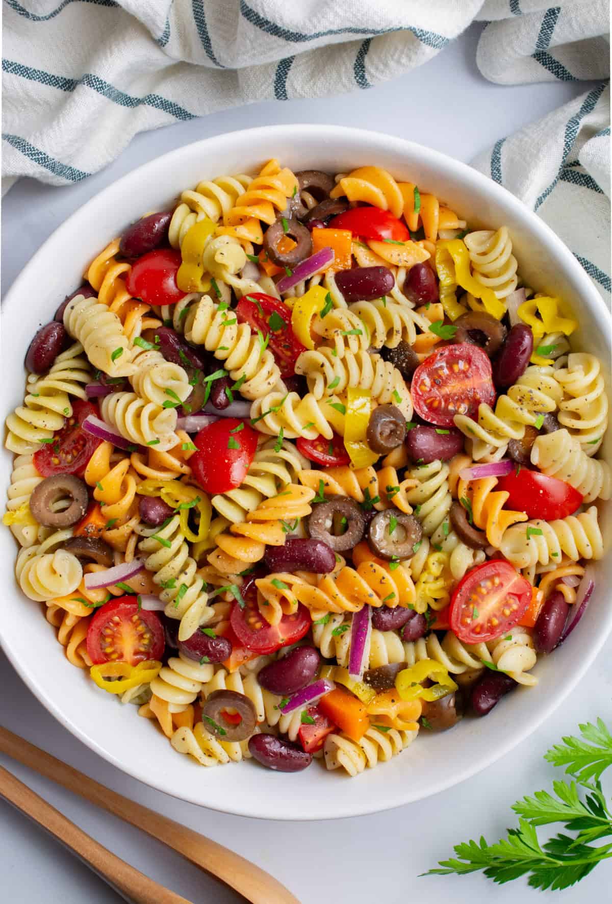 Looking down on a bowl of vegan Italian pasta salad with wooden tongs.