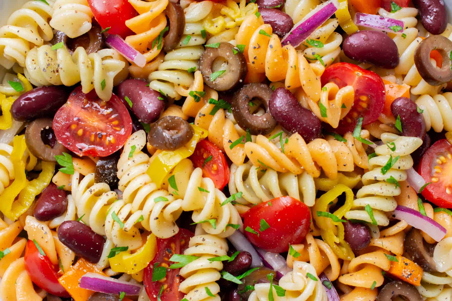 vegan pasta salad with tri-color pasta, grape tomatoes, sliced olives, red onion, pepperoncini, and kidney beans.
