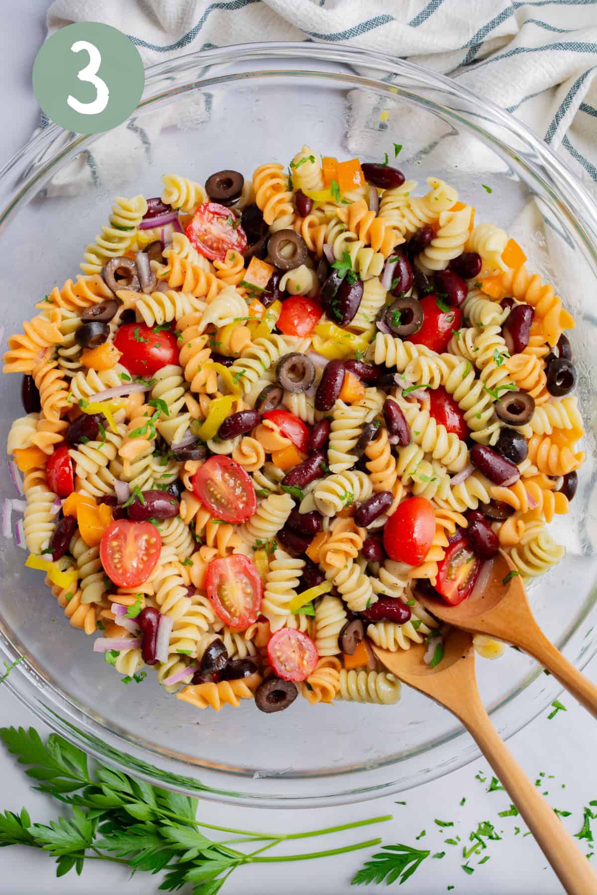 A large glass bowl of mixed pasta and veggies with Italian vinaigrette. 