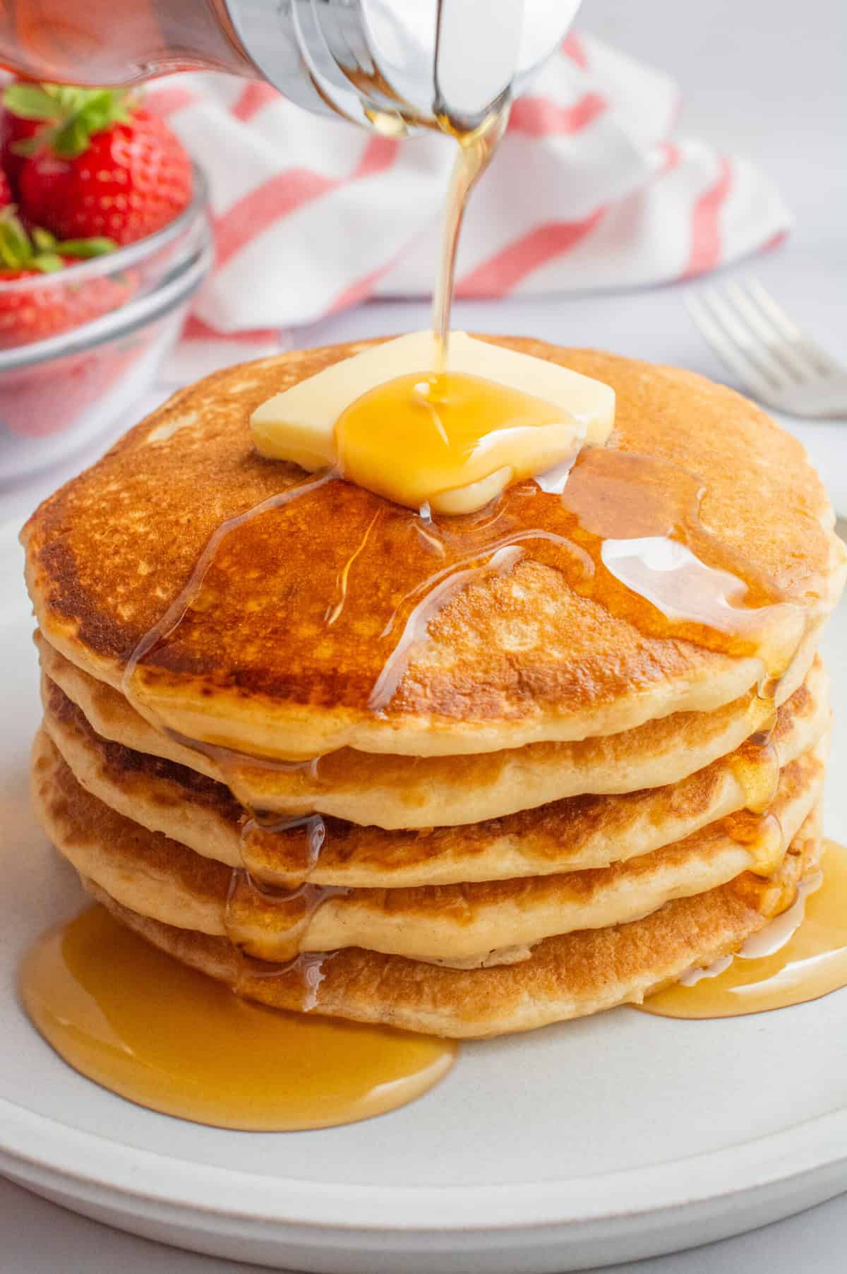 Syrup being poured on a stack of vegan buttermilk pancakes topped with butter.