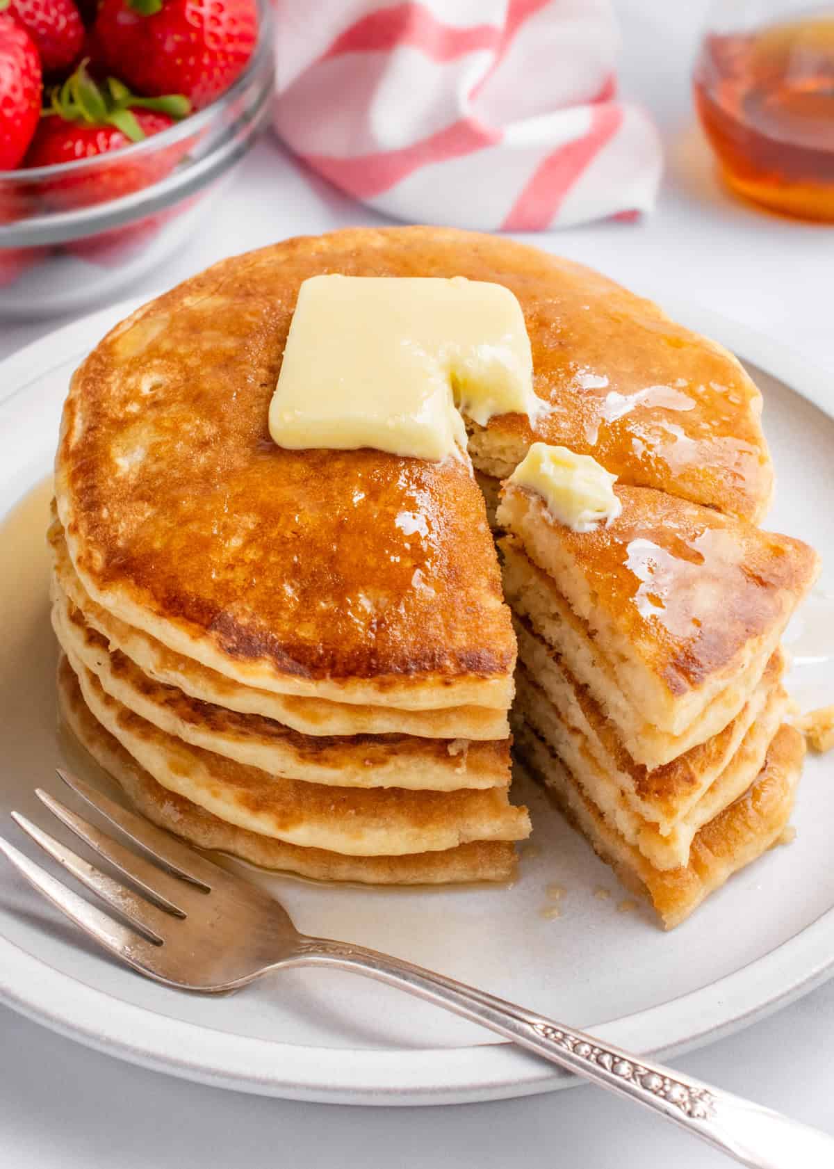 A stack of 5 vegan pancakes topped with butter and syrup cut into.