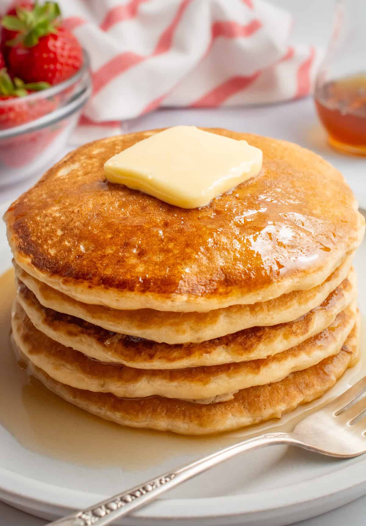 A stack of vegan buttermilk pancakes topped with butter and maple syrup.