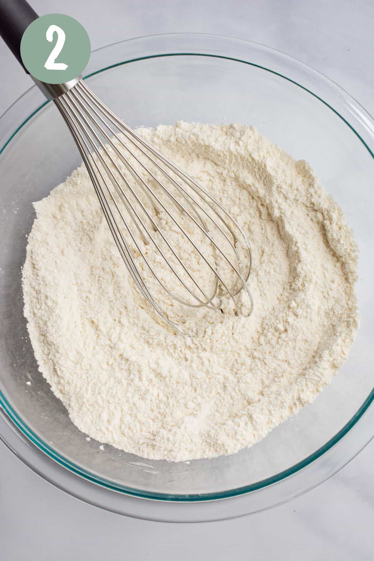 A bowl of dry ingredients with a large whisk.