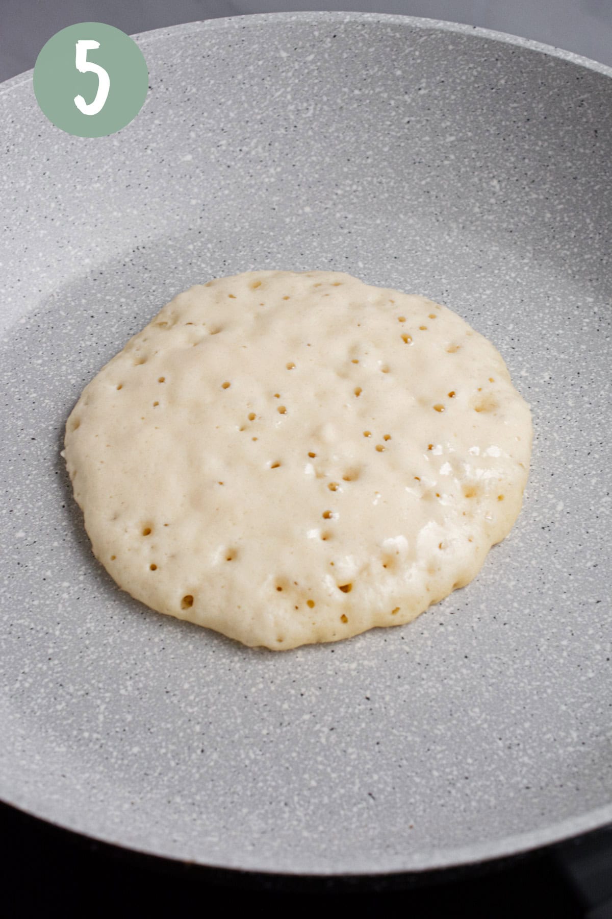 Pancake batter on a pan with bubbles forming.