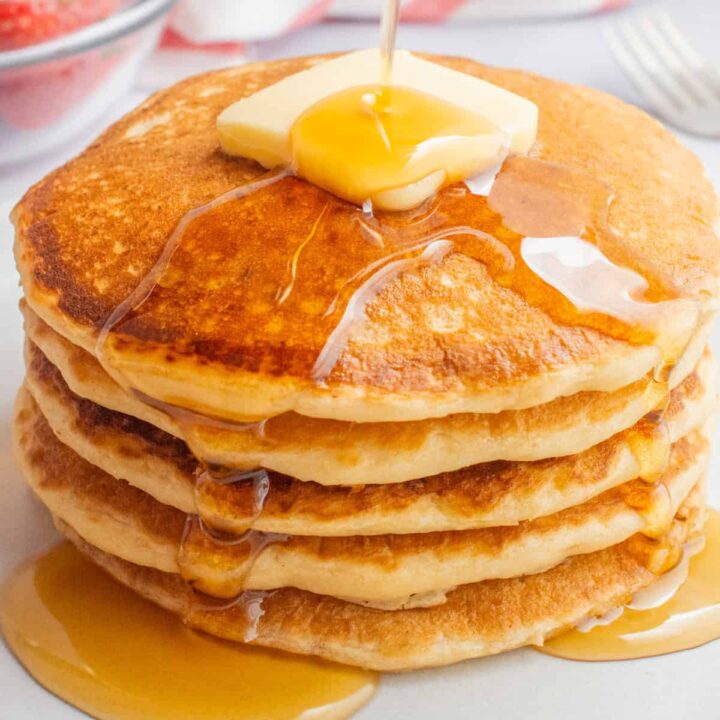 A stack of vegan buttermilk pancakes topped with butter and drizzled with syrup.A stack of vegan buttermilk pancakes topped with butter and drizzled with syrup.