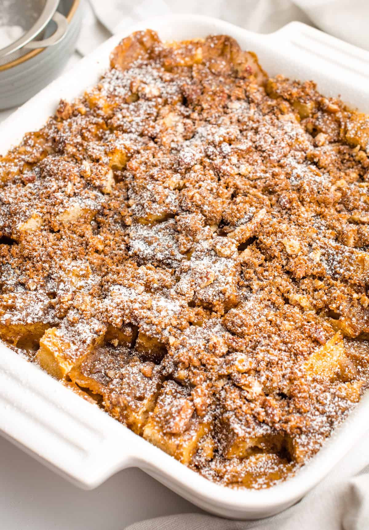 French toast casserole topped with powdered sugar in a white casserole dish.
