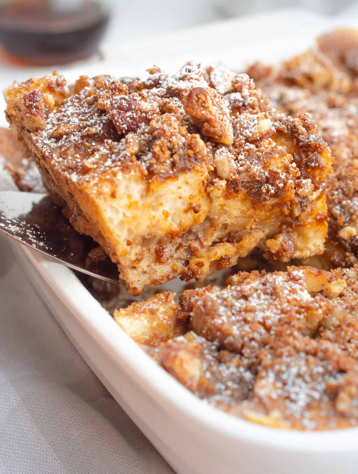 A slice of baked french toast being removed from the casserole dish.