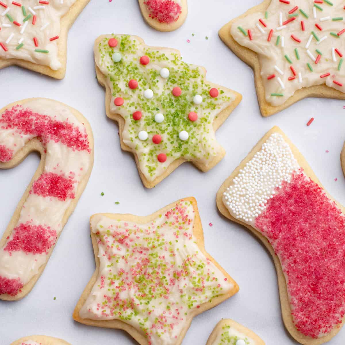 Decorated vegan sugar cookies cut into Christmas trees, stockings, candy canes, and stars.