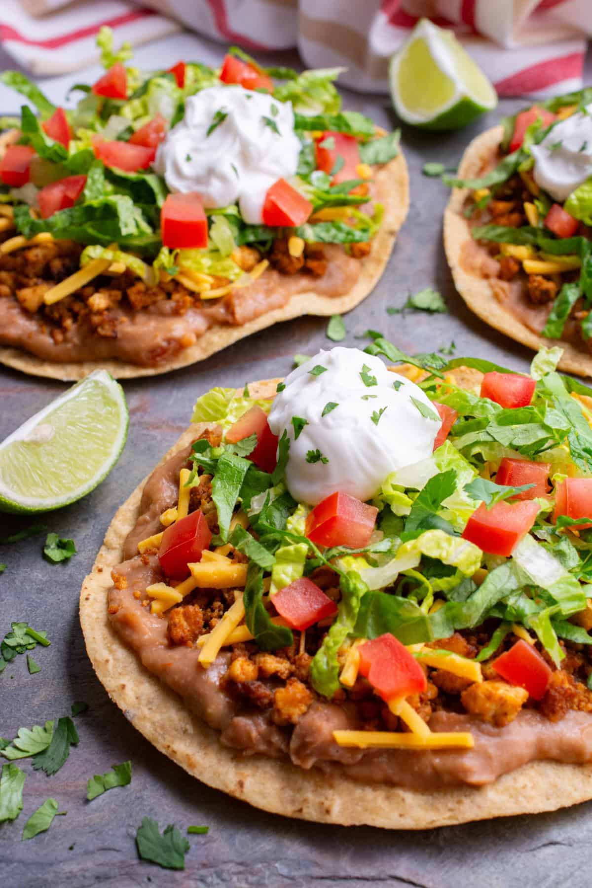 Vegan bean and tofu ground beef tostada topped with lettuce, sour cream, and diced tomatoes.