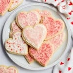 Heart-shaped sugar cookies with frosting and sugar sprinkles on a plate.