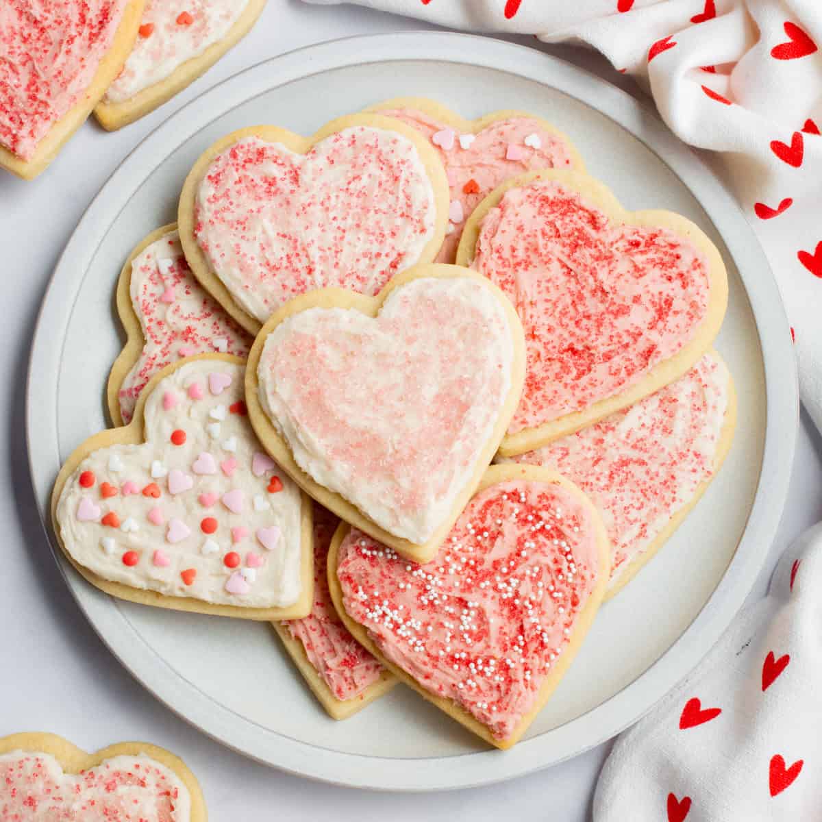 Heart-shaped sugar cookies with frosting and sugar sprinkles on a plate.