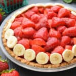 Fresh strawberry pie lined with banana slices with a walnut crust in a glass dish.