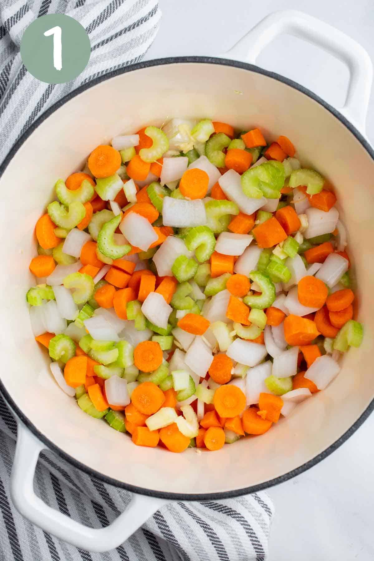 A white soup pot with chopped veggies.