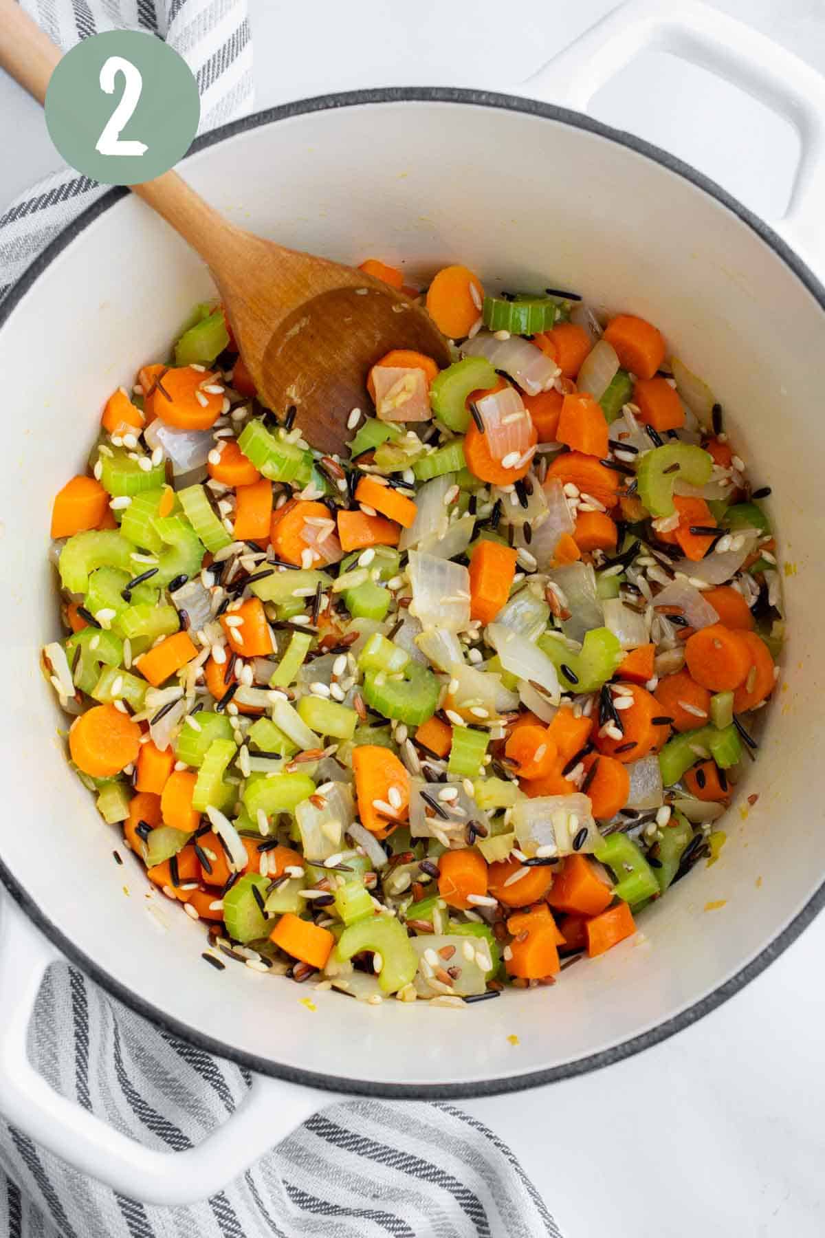 A white soup pot with chopped veggies and a wild rice blend.