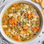 A bowl of soup with wild rice, white beans, carrots, onions, and celery.