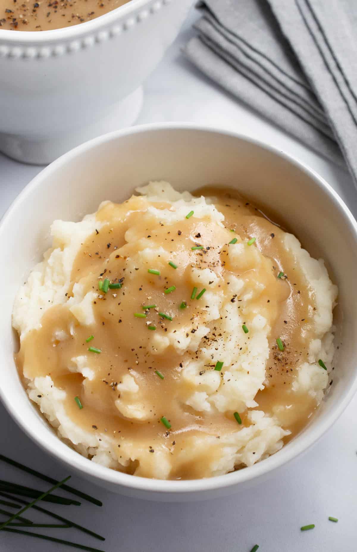 A white bowl of mashed potatoes topped with onion gravy, chives, and black pepper.