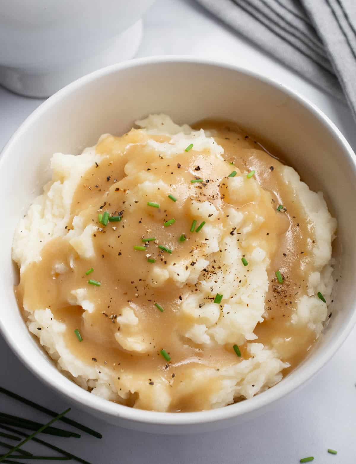 Mashed potatoes and gravy in a white bowl with a gravy boat nearby.