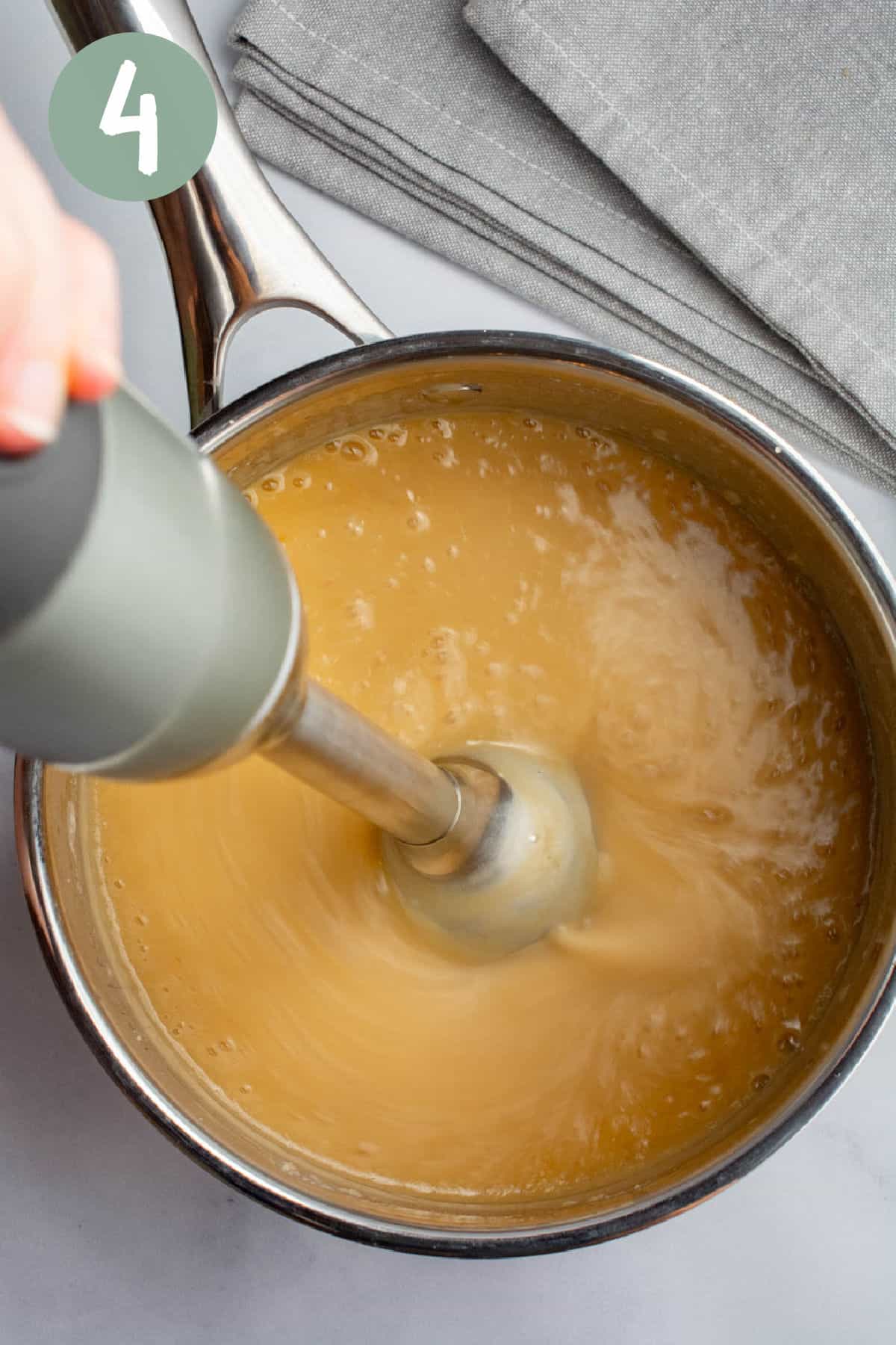 Onion gravy is being blended with an immersion blender in a saucepan.