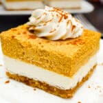 Vegan cheesecake bar with walnut crust, a plain cheesecake layer, and a pumpkin cheesecake layer topped with coconut whip.