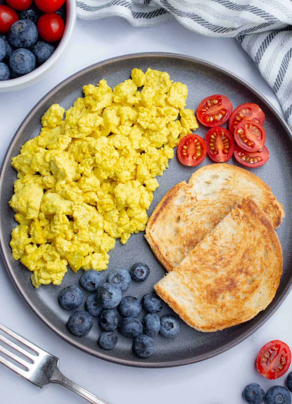 A plate of tofu scramble, toast, blueberries, and cut cherry tomatoes.