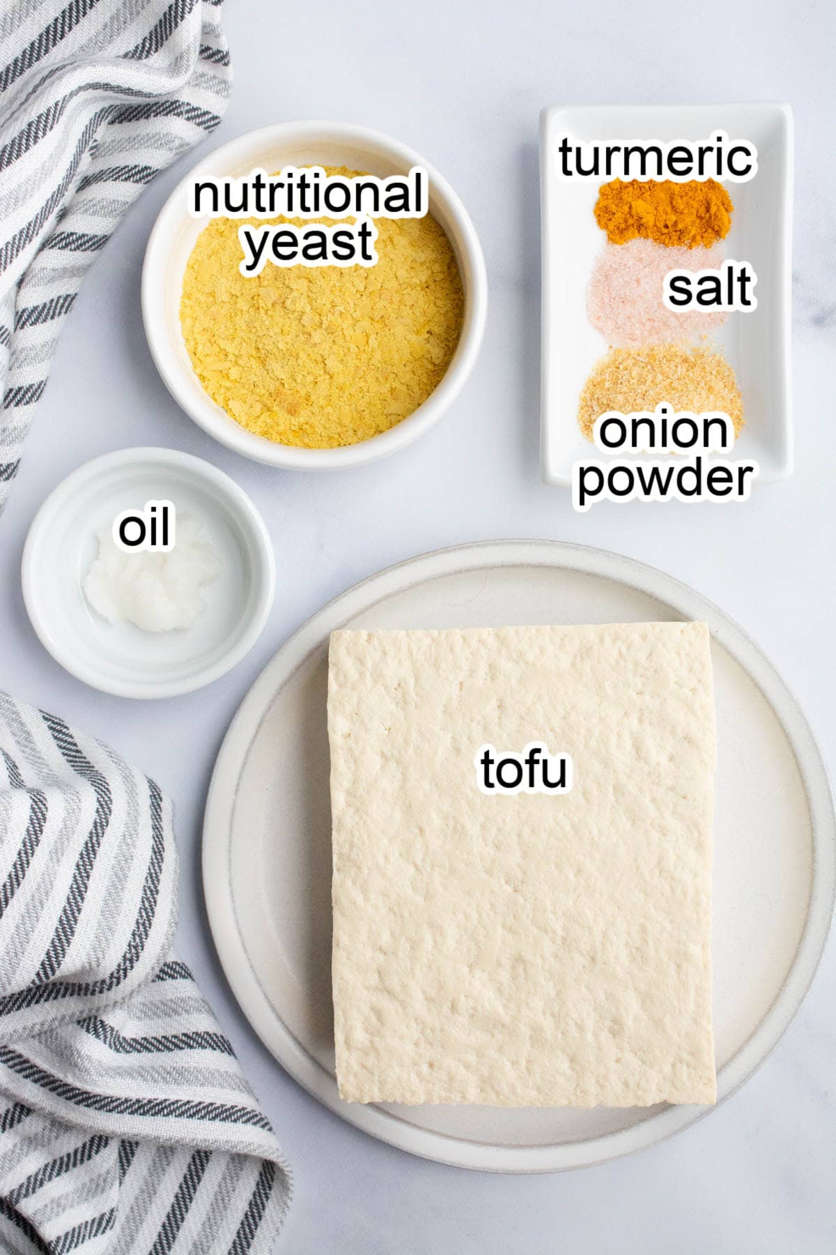 Raw tofu on a plate surrounded by bowls of spices.