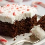 A slice of chocolate cake with white frosting, topped with crushed peppermint candy canes